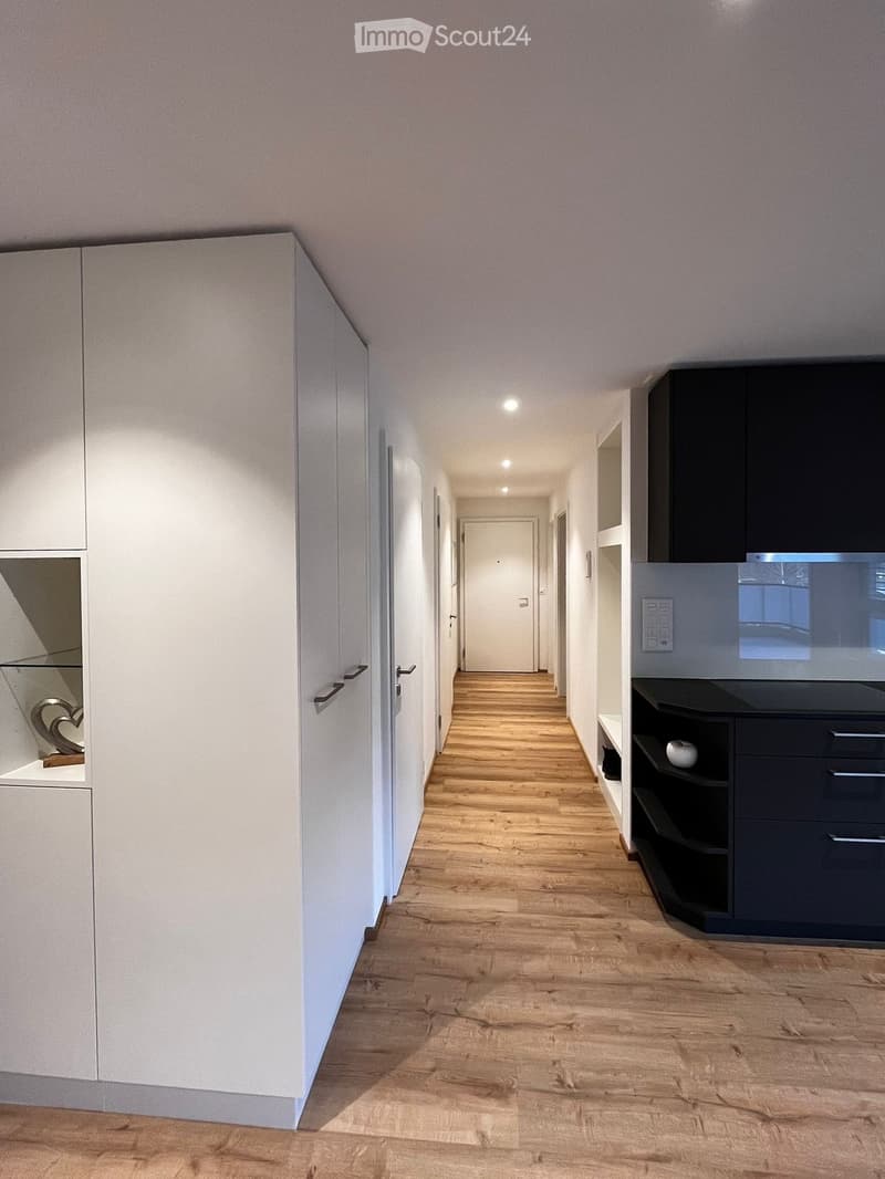 long hallway with wooden floor, white cabinets on left, black cabinets and drawers on right