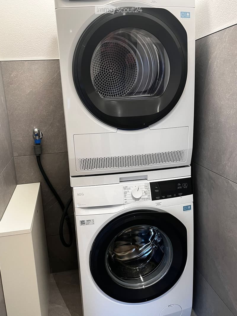 Stacked washing machine and dryer in a small room, gray tiled walls, white cabinet