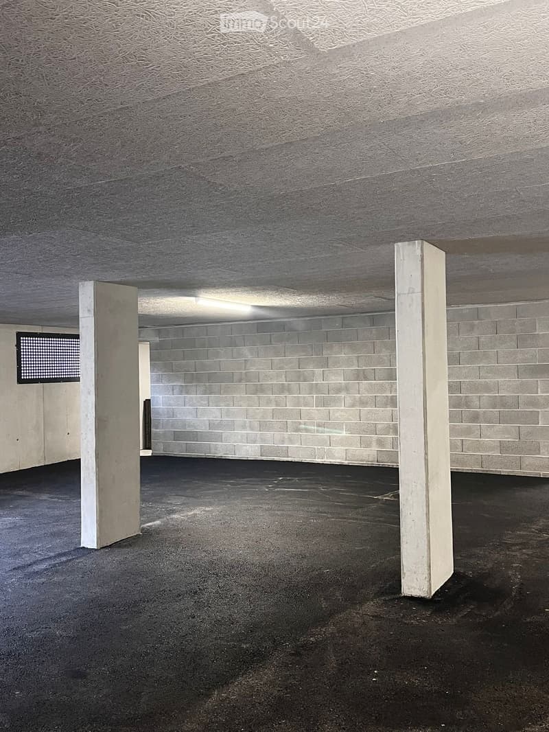 A basement parking area with a ceiling, columns, and a floor. White walls, a brick wall, and a window.