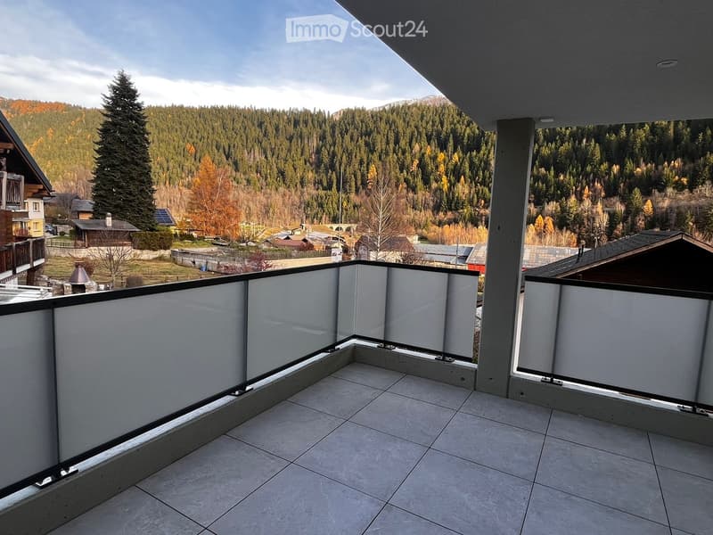 balcony with tiled flooring, glass railings, view of a wooded hillside