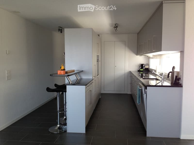 Modern kitchen with white cabinets, black countertops, and stainless steel appliances. Features a bar area with stools and a small table.