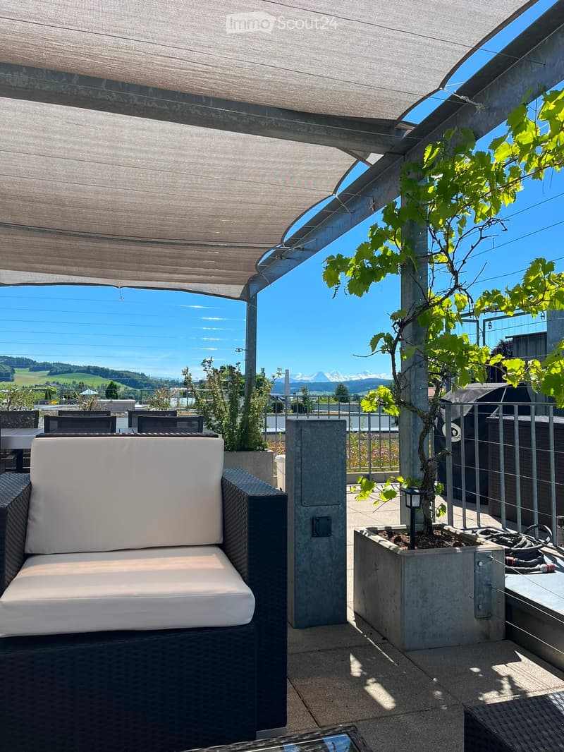 Modern outdoor seating area with a white cushioned sofa, a small table, and a potted plant, featuring a scenic mountain view.