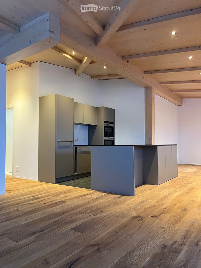 Modern kitchen with light wood beams on the ceiling, light-colored cabinets, stainless steel appliances, and a central island.