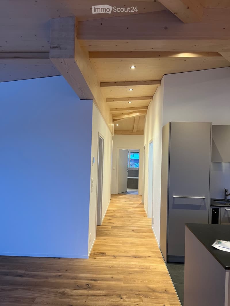 Modern hallway with wooden flooring, white walls, and recessed lighting. Features a large window on the left and a door leading to another room at the end.
