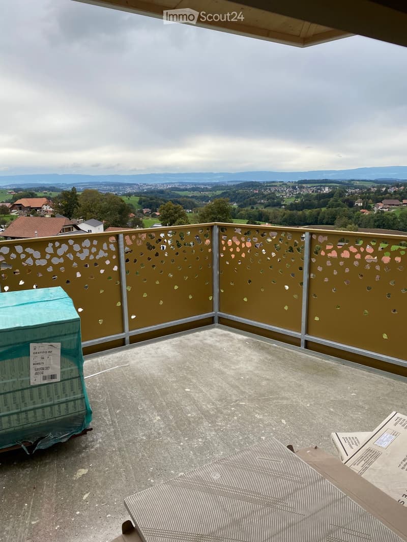 Roof terrace with metal railing featuring decorative cutouts, overlooking a scenic valley and town with houses and greenery.