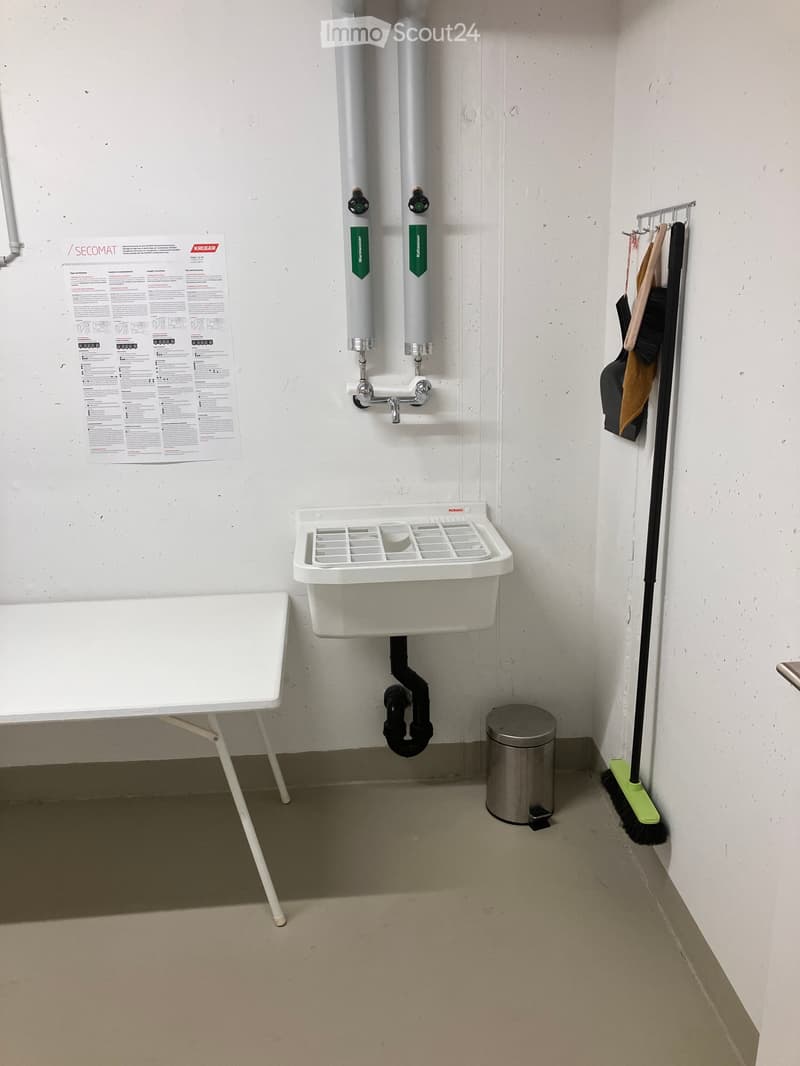 A small, functional bathroom with a white sink, bathtub, coat rack, and cleaning tools.