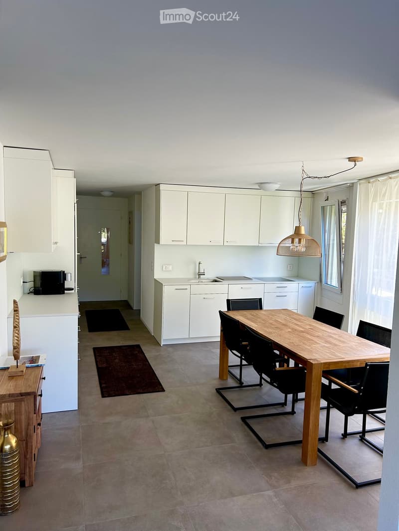 Modern kitchen and dining area with white cabinets, a wooden dining table, black chairs, and a coffee maker on the counter.