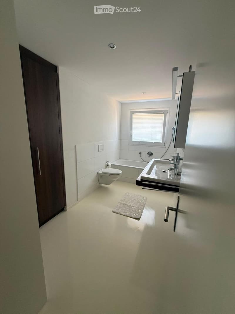 Modern bathroom with white tiles, a toilet, a sink with a mirror, a bathtub, and a small rug on the floor.