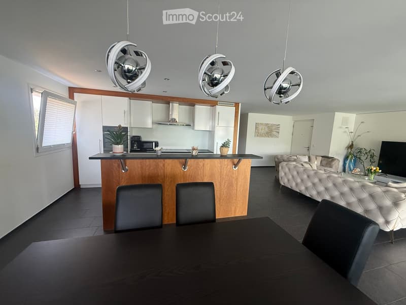 Open-plan living and dining area with a modern sofa, dining table, chairs, and a kitchen island with pendant lights and a microwave.