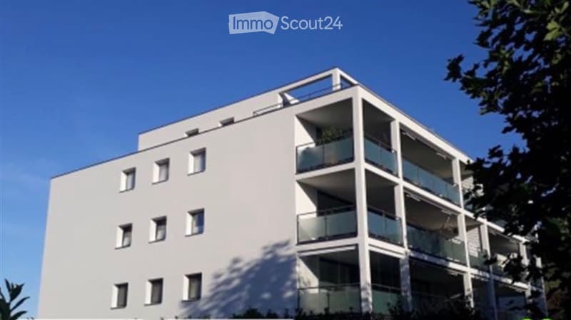 Modern multi-story apartment building with white facade, multiple balconies, and large windows.