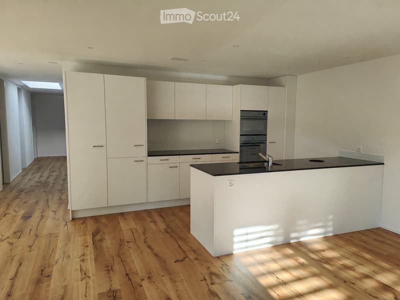 Modern kitchen with white cabinets, black countertops, and a central island. Features a wooden floor and built-in appliances.