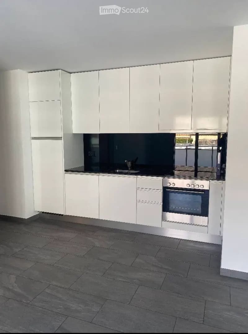 Modern kitchen with white cabinets, stainless steel oven, and dark tiled floor.