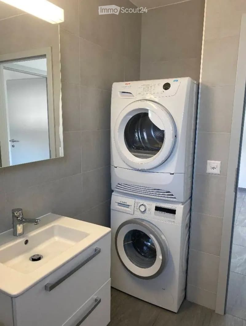 Modern bathroom with a white sink, chrome faucet, mirror, and stacked washing machine and dryer unit.