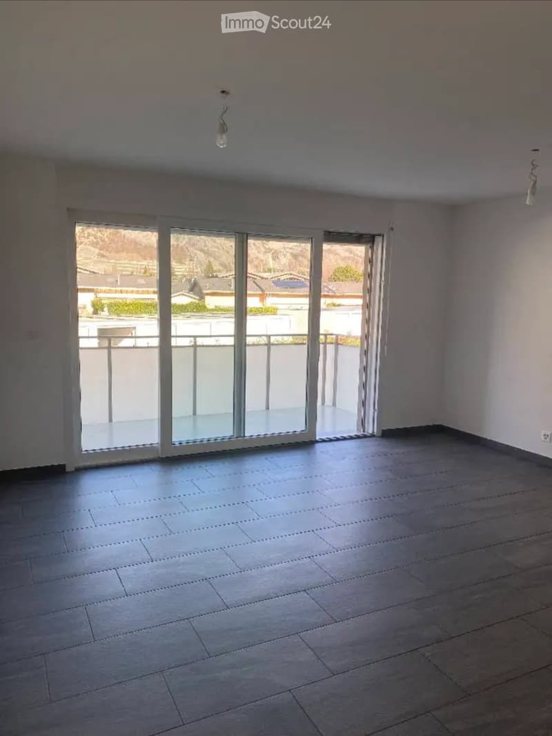 Empty room with tiled floor, white walls, and large sliding glass doors leading to a balcony.