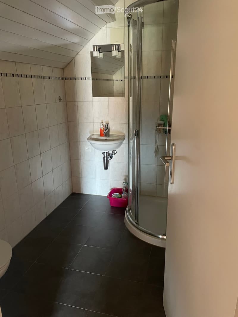 Modern bathroom with white tiles, black floor tiles, a white sink, a mirror, a shower, and cleaning supplies on the floor.