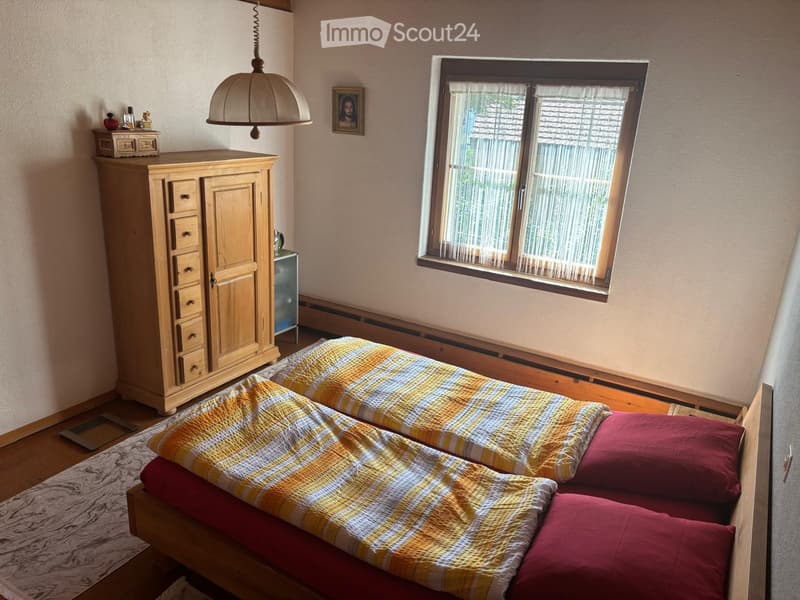 Cozy bedroom with two single beds, a wooden wardrobe, a hanging lamp, and a window with blinds.