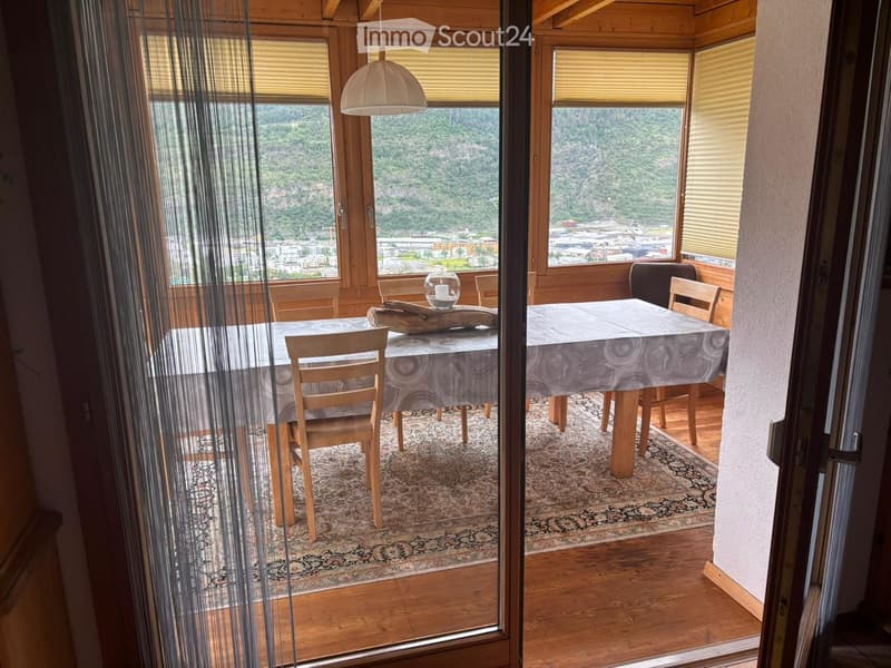 Dining area with wooden tables, chairs, and a scenic mountain view through large windows.