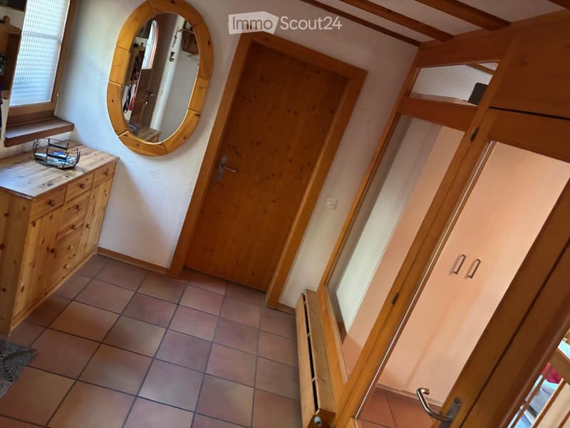 A narrow hallway with wooden doors, a round mirror, a small wooden cabinet, and a window with blinds.
