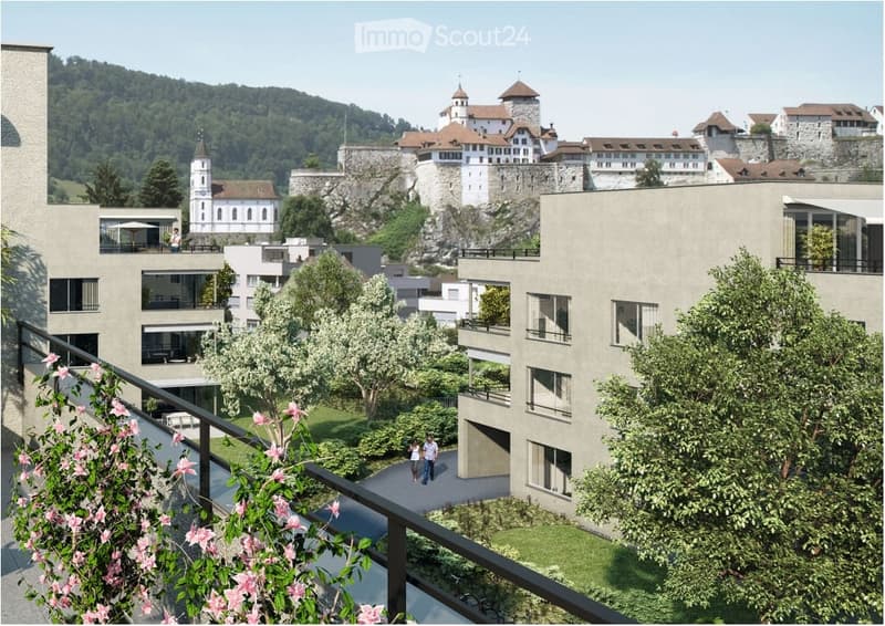View from a balcony overlooking a modern residential complex with surrounding greenery and a historic castle in the background.