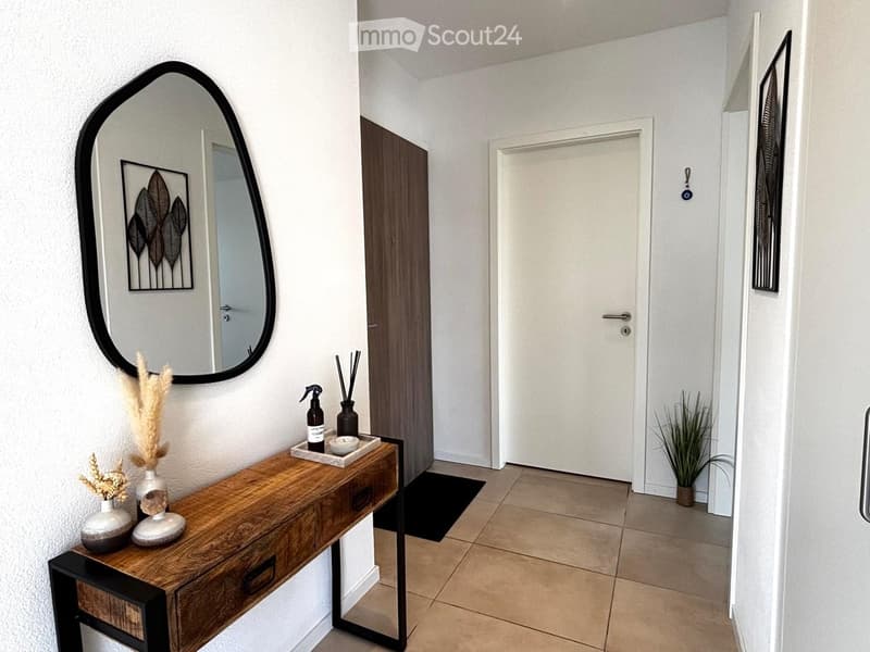Modern hallway with a wooden console table, decorative items, a large oval mirror, and a closed door leading to another room.