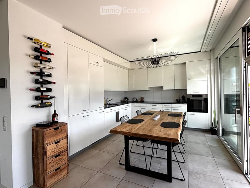 Modern kitchen with white cabinets, a wooden dining table, wine rack, and a large window.