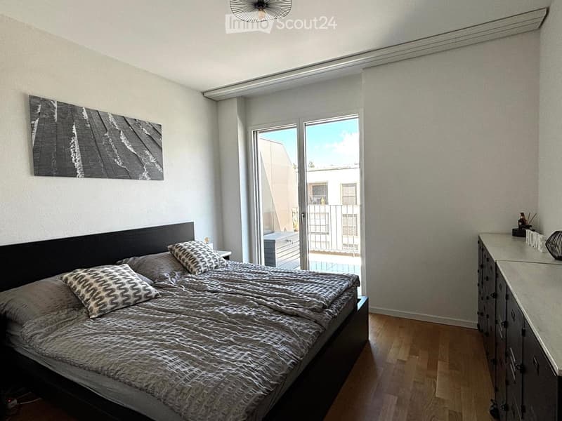 Modern bedroom with a large bed, patterned bedding, nightstand, dresser, and artwork on the wall. Features a sliding glass door leading to a balcony.