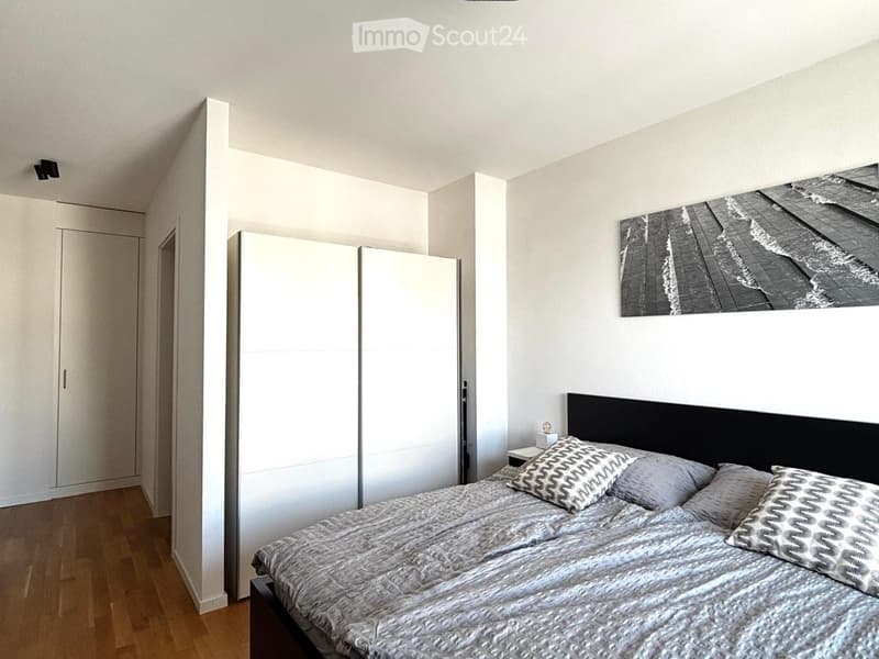 Modern bedroom with a large bed, nightstand, wardrobe, and a large picture frame on the wall.
