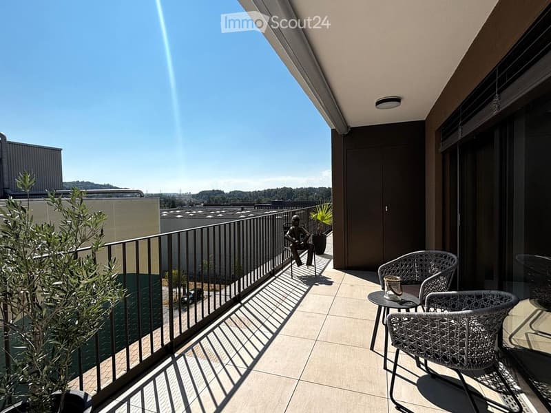Balcony with tiled floor, metal railing, two wicker chairs, small table with a cup, and potted plants.