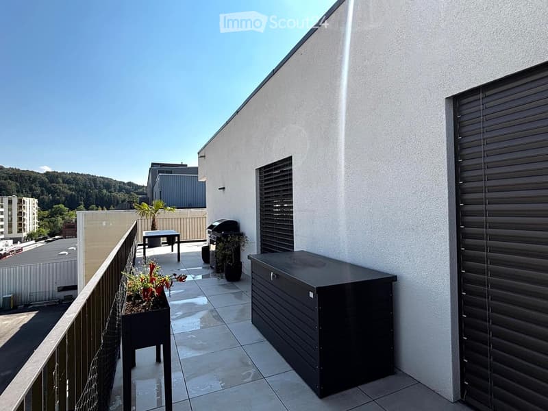 Modern rooftop terrace with tiled flooring, black table, grill, and potted plants, overlooking a cityscape with buildings and greenery.