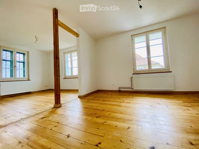 Empty room with wooden flooring, white walls, and multiple windows with blinds. Radiators are visible under the windows.