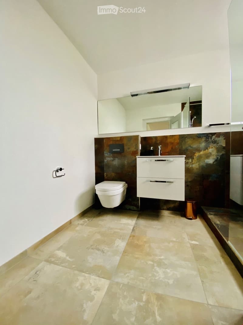 Modern bathroom with beige tiled floor, white toilet, white sink with mirrored cabinet, and dark brown accent wall.