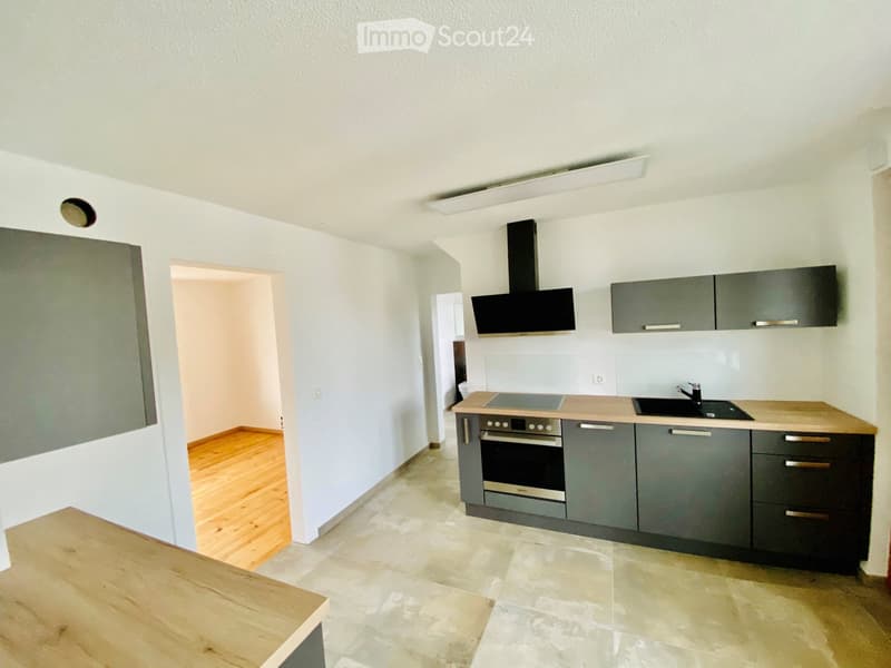 Modern kitchen with grey cabinets, stainless steel oven, sink, and range hood. Light wooden countertops and tiled floor.