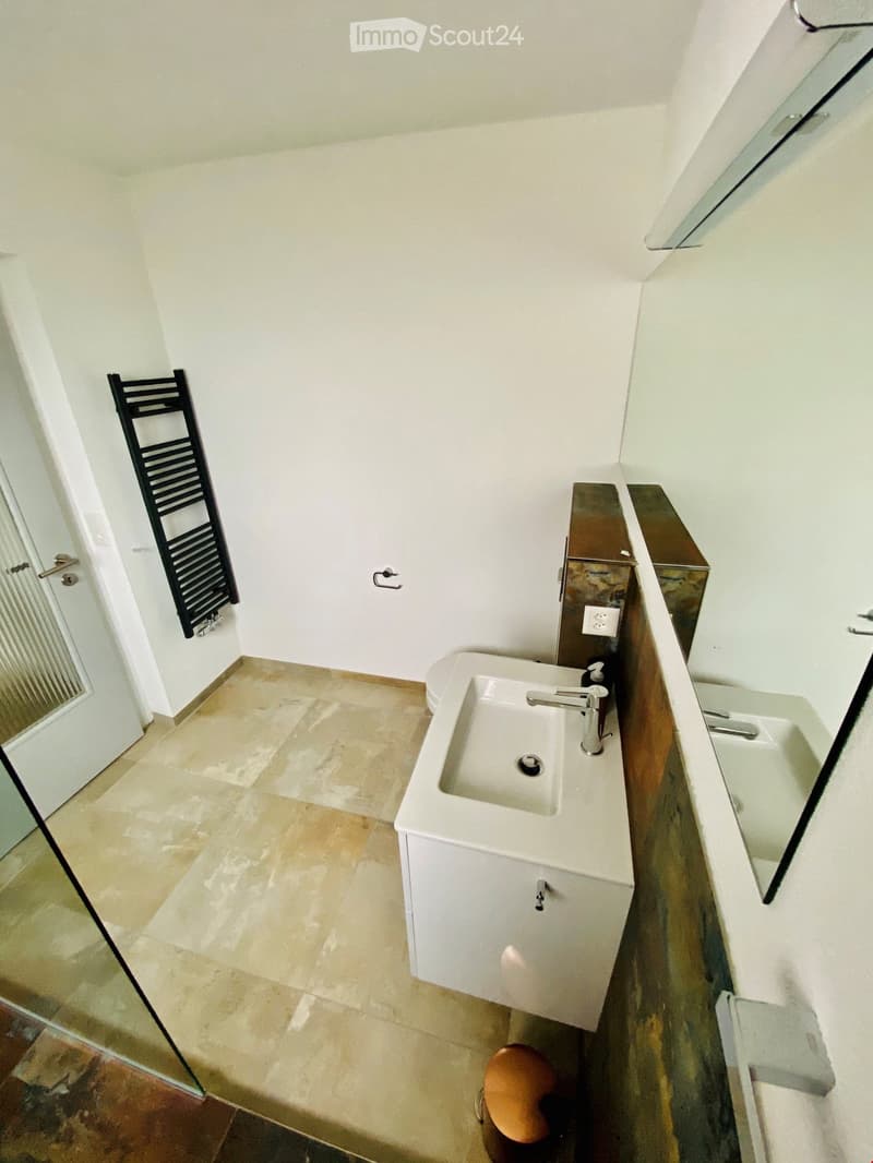 Modern bathroom with a white sink, chrome faucet, mirror, towel rack, and a small wooden stool.