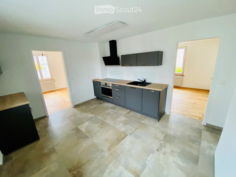 Modern kitchen with grey cabinets, a central island, and a tiled floor. Features include a sink, faucet, oven, and range hood.