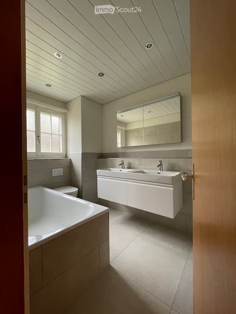 Modern bathroom with a white bathtub, double sink vanity, large mirror, and sleek fixtures.