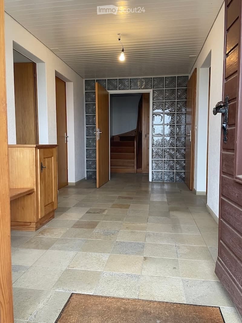Empty hallway with tiled floor, wooden doors, and a staircase leading upwards.