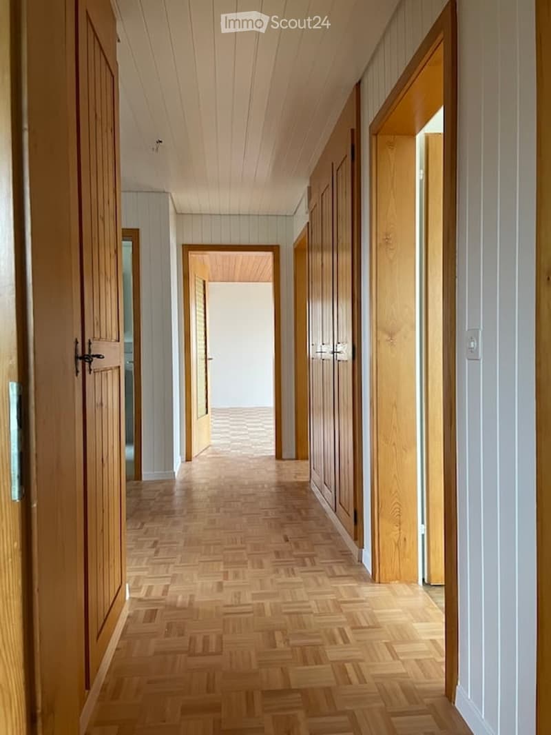 A long, narrow hallway with wooden flooring and white walls, featuring several open wooden doors leading to other rooms.