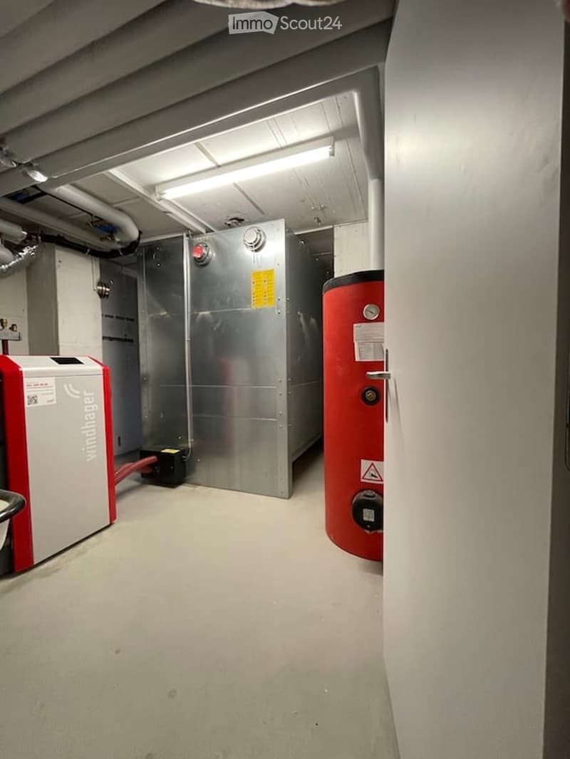 Utility room with a water heater, boiler, and electrical panel. The room has a concrete floor and exposed pipes and ductwork on the ceiling.