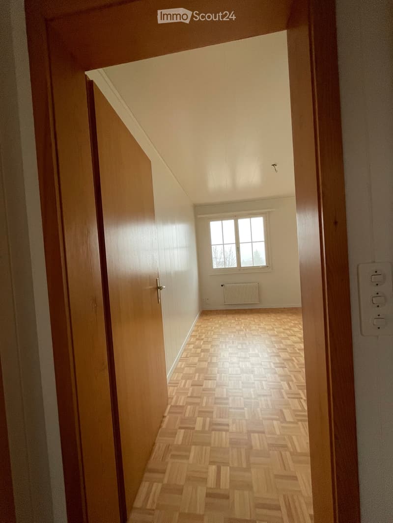 Empty hallway with wooden flooring, white walls, and a window at the end.