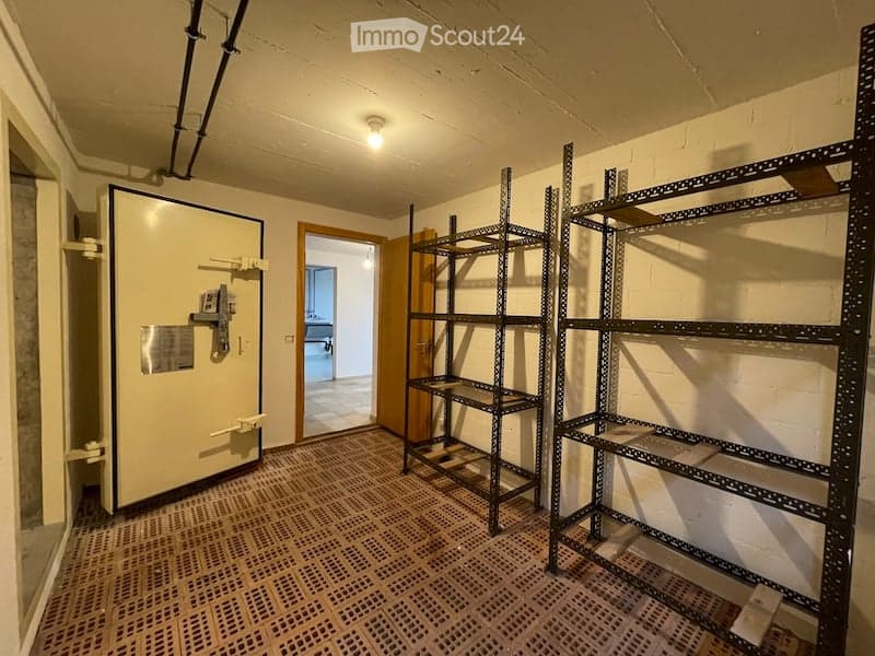 Empty room with metal shelving units, a large metal door, and a visible adjacent room through an open doorway.