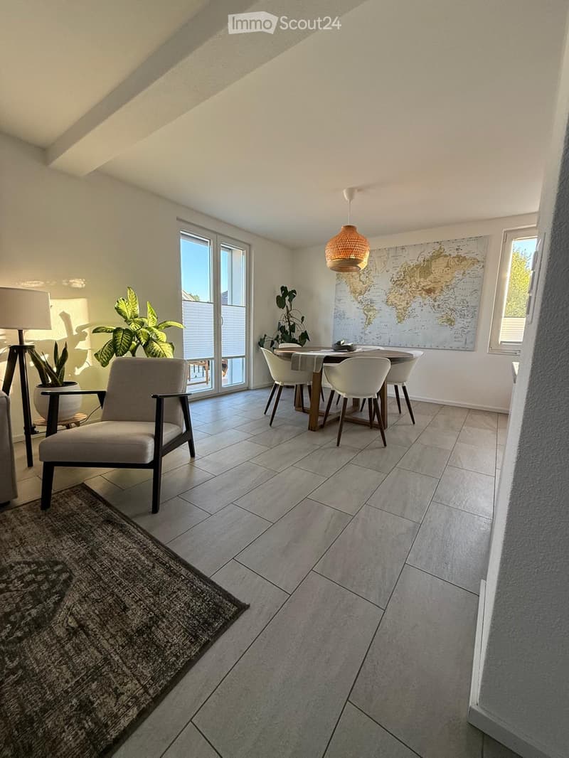 Bright, modern living space with a dining area, a comfortable armchair, a pendant light, and a world map on the wall.