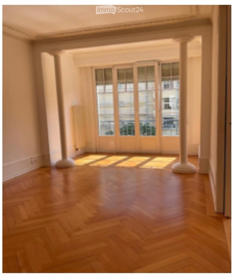 Empty room with wooden flooring, large windows, and white columns. No furniture or equipment present.