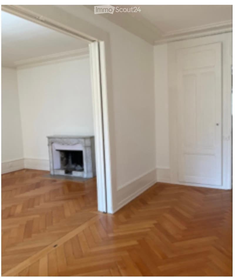 Empty room with wooden herringbone flooring, white walls, and a fireplace with a decorative mantel.