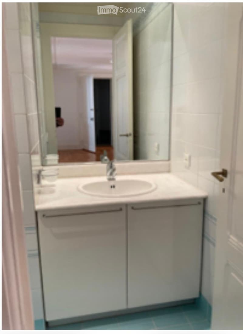 Bathroom with a white sink, mirror, and cabinets, featuring light blue tiled flooring.