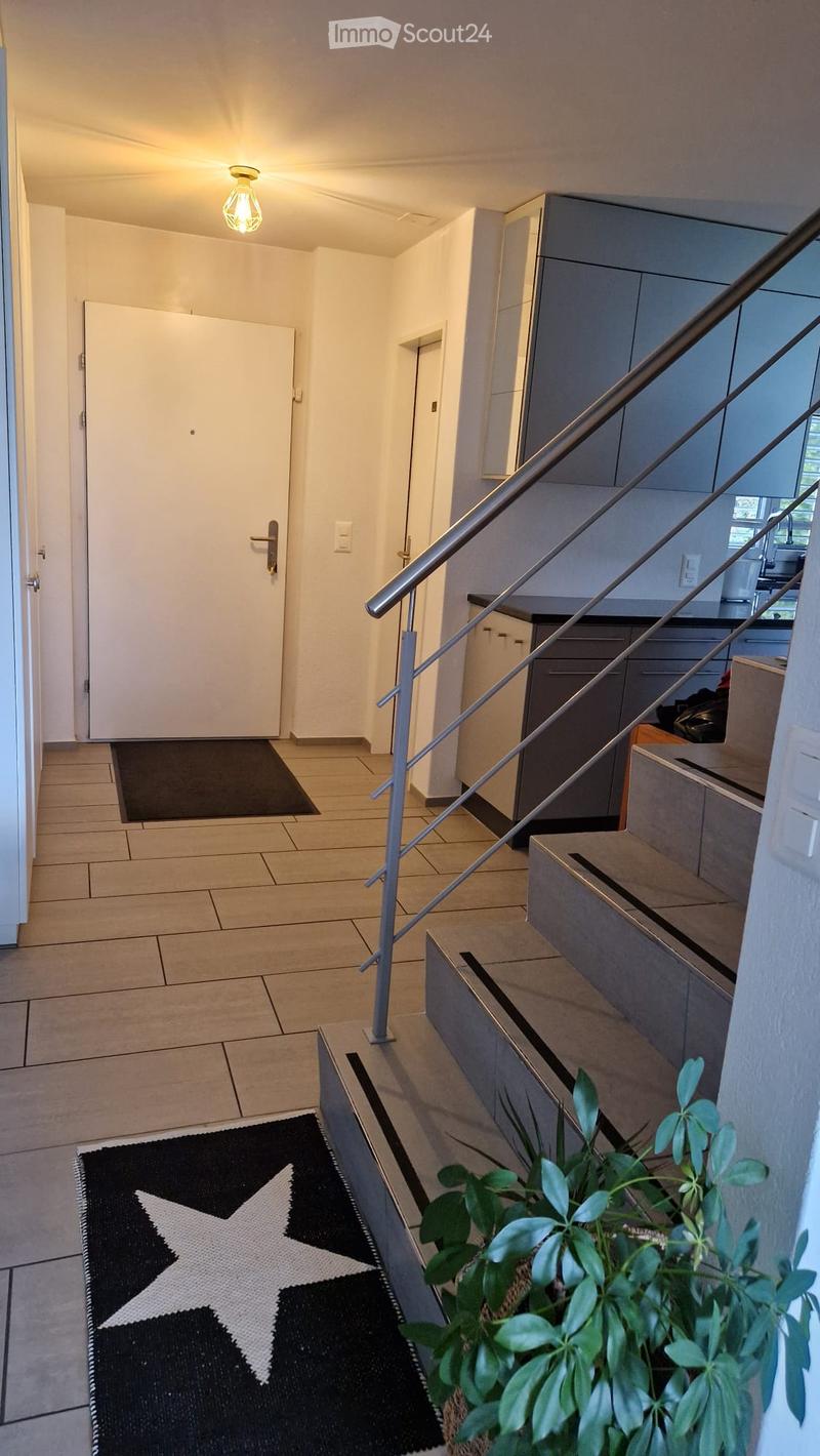 Modern hallway with tiled floor, staircase with metal railing, and a small plant in the foreground.