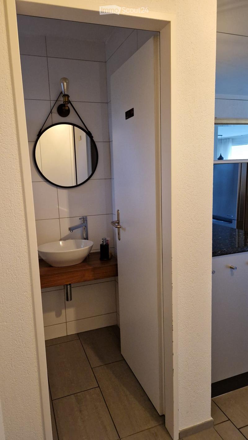 Modern bathroom with a white sink, chrome faucet, round mirror, and soap dispenser on a wooden countertop.