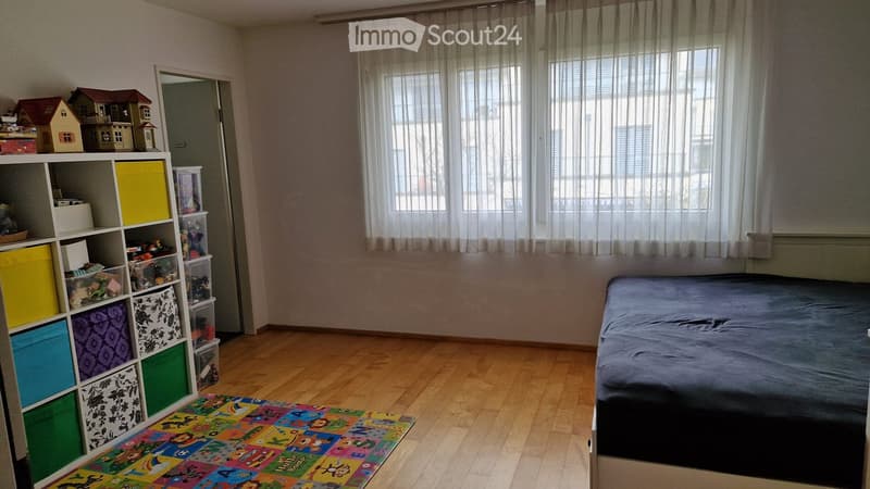 Child's bedroom with a bed, colorful storage shelf, toy house, and play mat on the floor.