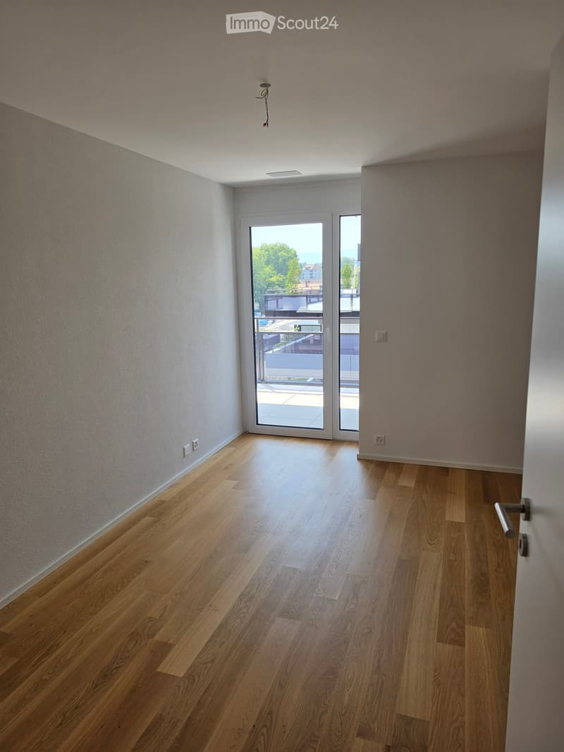 Empty room with wooden flooring, light-colored walls, and a large sliding glass door leading to a balcony.