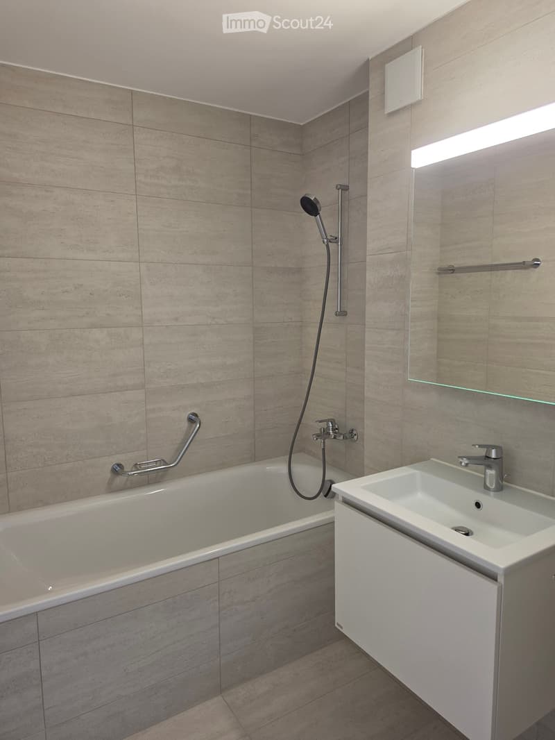 Modern bathroom with a bathtub, sink, and showerhead, featuring beige tiled walls and a large mirror.