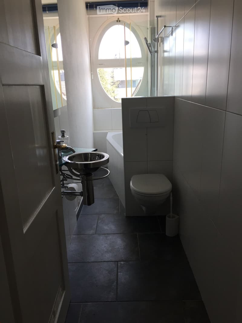 Modern bathroom with dark tiled floor, white walls, bathtub, toilet, sink, and glass shower enclosure.